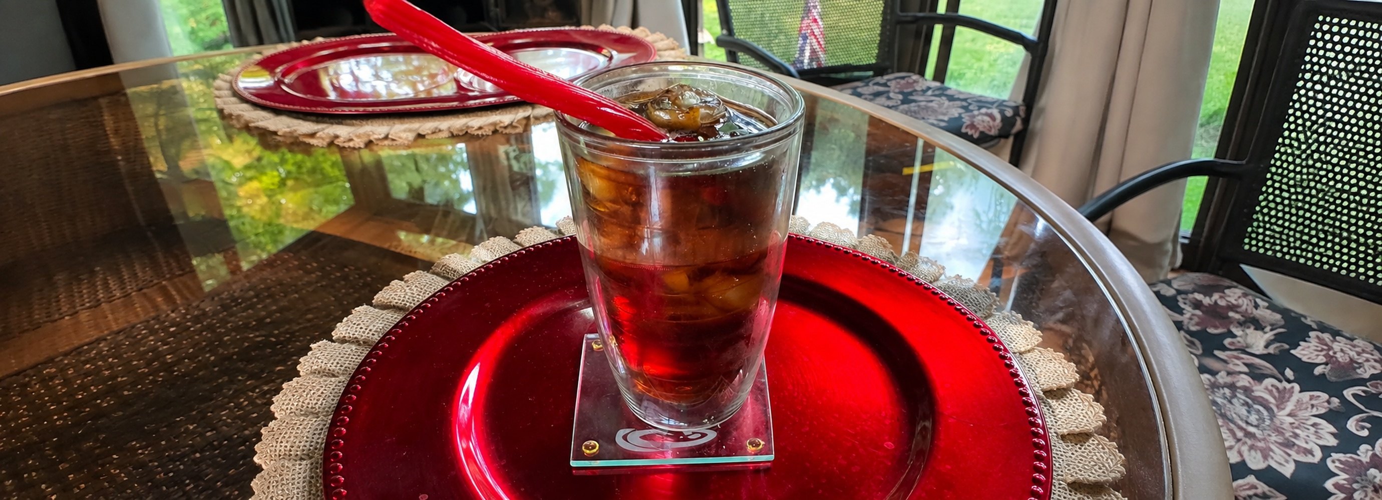 Glass of cherry coke on a red plate.