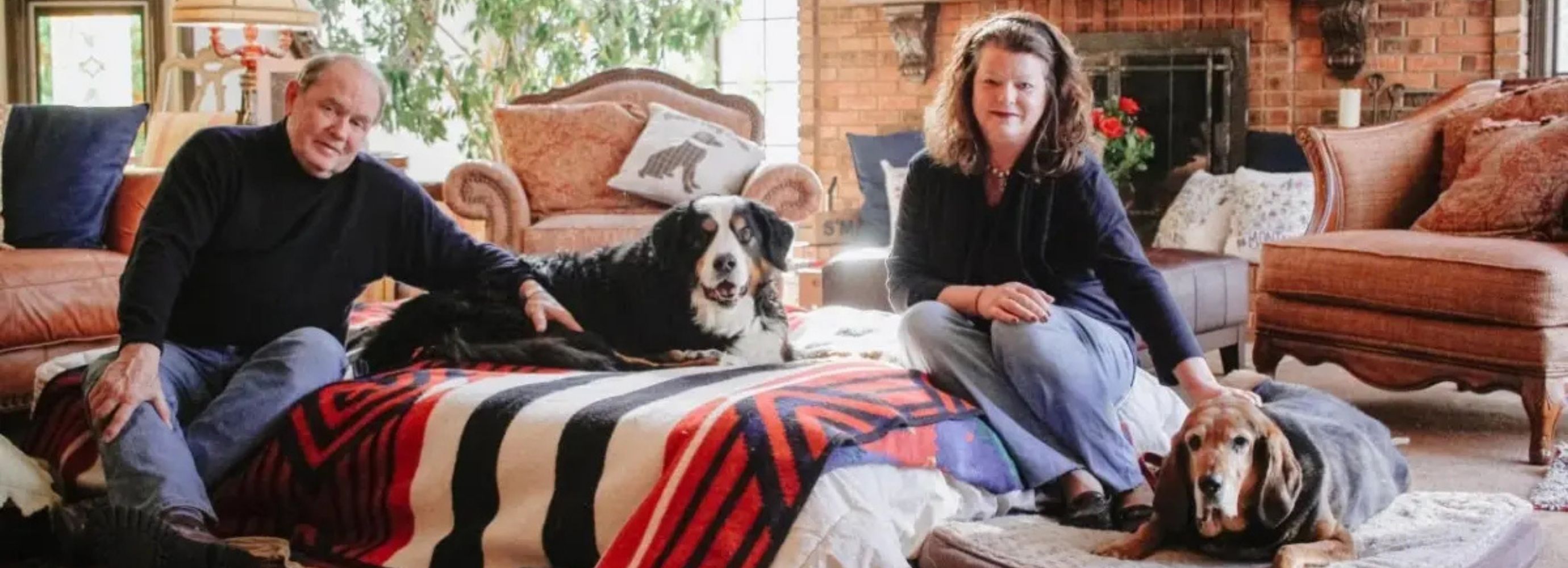 A man and a woman sitting in a living room with two dogs.