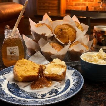 A table with corn bread muffins, butter, and honey.