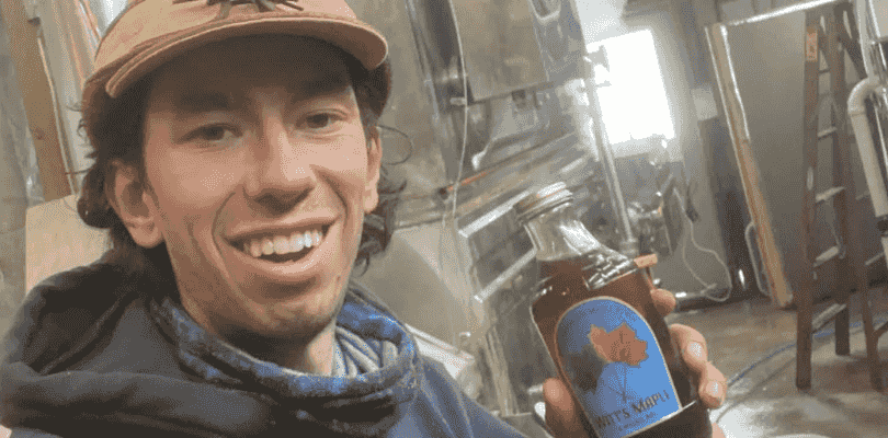 Man smiling in factory holding Witt's Maple Syrup bottle.