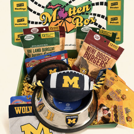 Gift box filled with University of Michigan themed gifts for dogs, including a dog bowl, toys, and snacks.